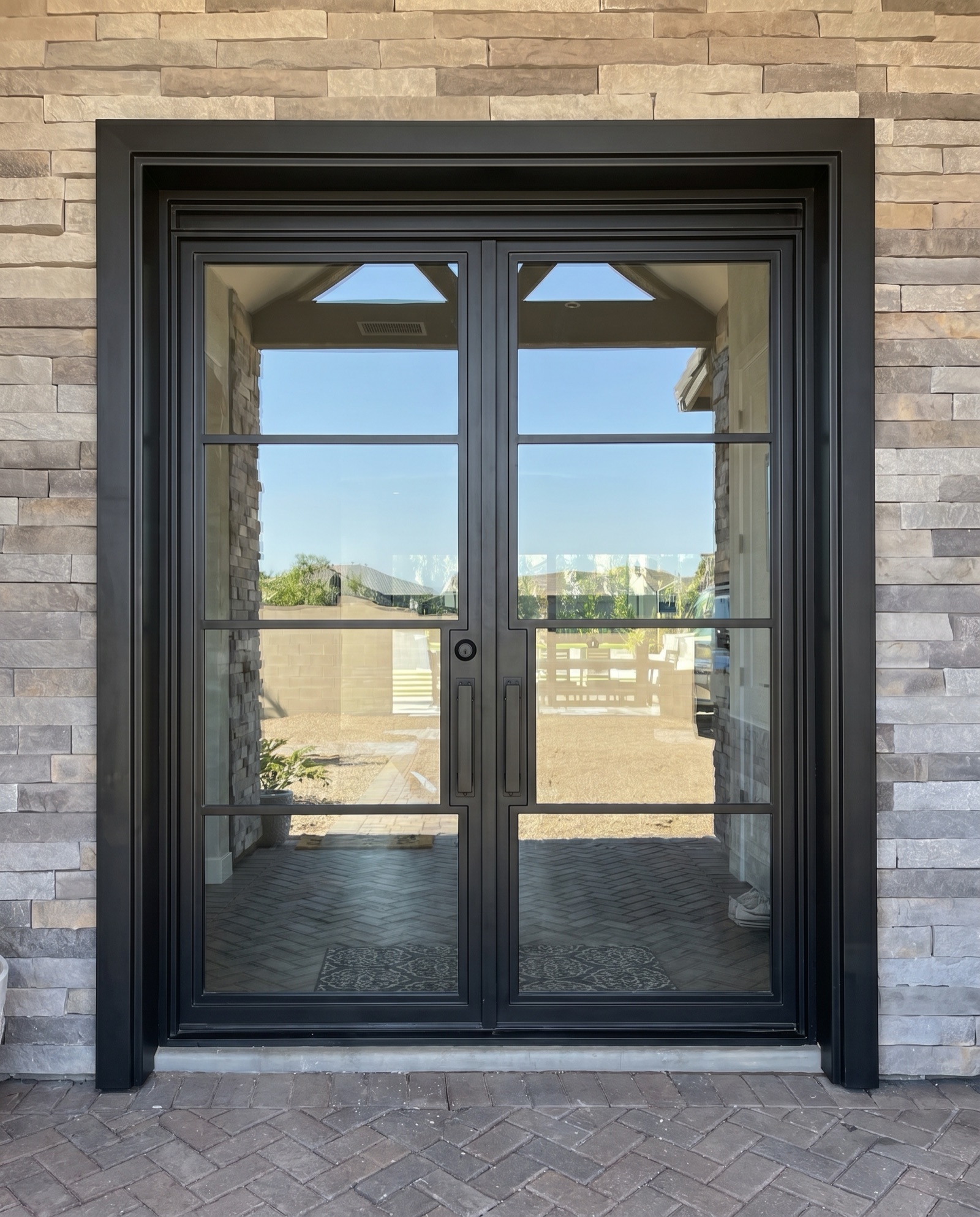 Black steel-grid glass entry door on a stone facade by Mad Touch Glass